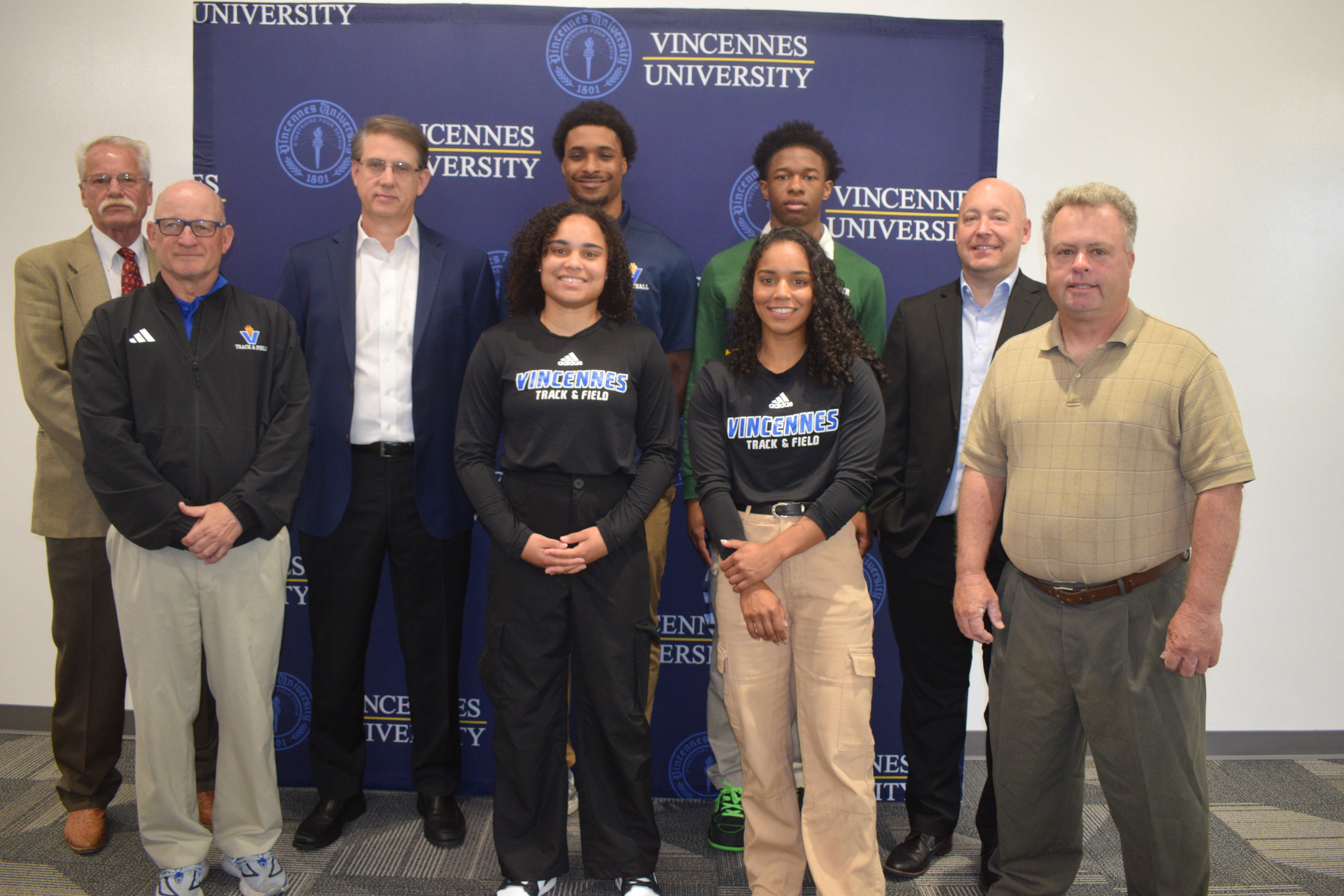 A group of VU student-athletes, VU coaches and VU Board Chairman Mike Sievers stand in front of a VU step and repeat backdrop.